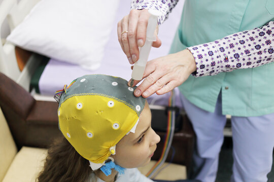 Girl before procedure electroencephalography, nurse using syringe introduces special gel for electrodes located in cap of electroencephalogram