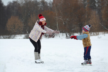 Happy mother and her cute little son skate on ice in winter day