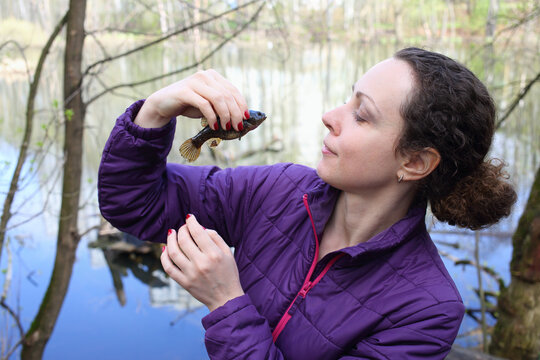Woman with a fish in her hands on a fishing trip near the pond with reflection of a multistory building