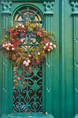 A wooden home door adorned with a wreath made of green flowers, adding a charming fixture to the...