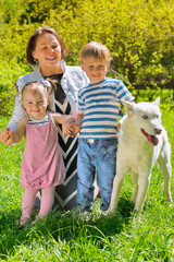 Obraz premium Mom with her daughter and son sitting with dog on grass in park