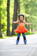 Little cute girl in skirt and helmet roller skates in garden at summer day