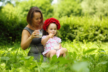 Little girl in flower wreath and her mother hold milk and thumb up in summer park