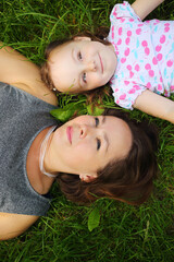 Little cute girl and her mother lie on grass and look up in park