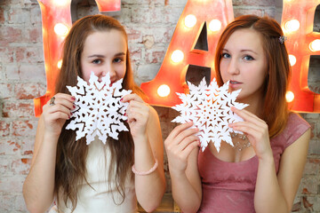 Two girls teenagers sit with paper snowflakes near illuminated letters in studio
