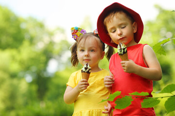 Happy little boy and girl eat sweet ice cream in green summer park