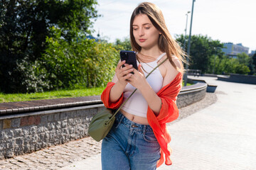 The girl is walking in the park looking at the phone. Modern woman on a walk