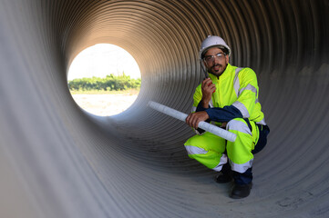 Smart engineer with safety suit holding walkie-talkie inspecting large power system pipeline.
