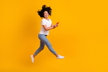 Fototapeta na wymiar Full length photo of good mood excited lady dressed white t-shirt jumping high typing gadget empty space isolated yellow color background