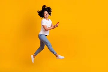 Foto op Canvas Full length photo of good mood excited lady dressed white t-shirt jumping high typing gadget empty space isolated yellow color background © deagreez