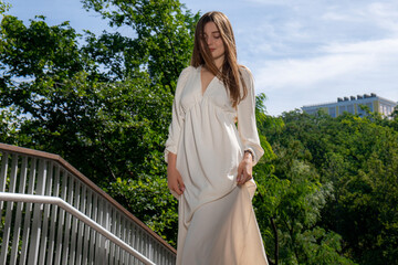 A beautiful girl in a white dress in full height against the background of a modern city. Green park