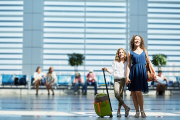 Smiling mother and daughter stand in waiting hall at airport