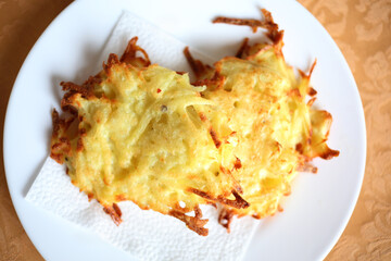 Yellow fresh potato pancakes are on white plate on table, closeup