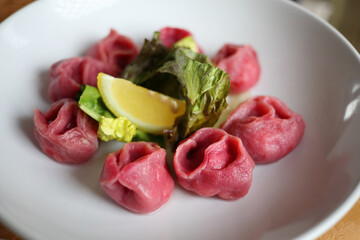 Red dumplings with salad and lemon are on white plate, close up