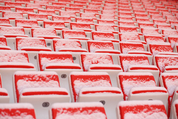 Rows of bright empty seats of grandstands covered by snow on stadium