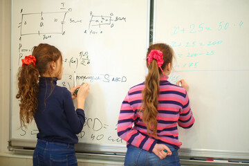 Schoolgirls write on blackboard with geometry examples and exercises in classroom, back view, text...
