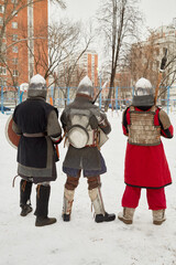 Three men dressed in defensive knight costumes stand in courtyard in winter