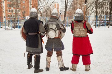 Three men dressed in defensive knight costumes stand in courtyard in winter