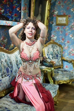 Woman dressed in oriental costume poses sitting on sofa in old-fashioned style room