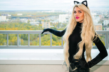 Pretty blonde woman with black cats ears poses on balcony at autumn day