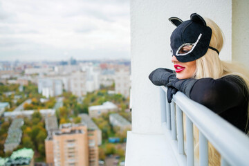 Pretty blonde woman with black cats looks down on balcony in city