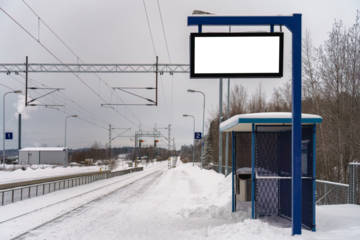 Empty train station platform on a snowy day, featuring a blue shelter and an empty billboard