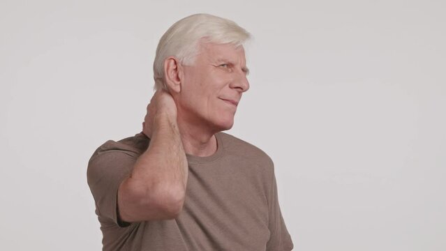 The elderly man winces in pain, clutching his neck with his arm