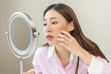 Dermatology, expression face worry asian young woman looking mirror hand touch facial at dark spot of melasma, freckles from pigment melanin, allergy sun. Beauty care, skin problem treatment, skincare