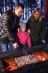 Family of three people doing barbecues on a winter evening