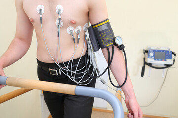 Patient with ECG electrodes on chest and an instrument for measuring blood pressure during exercise
