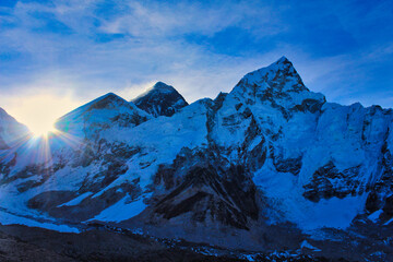 Dramatic scene of the sun rising behind Mount Everest with the summit, West shoulder and Nuptse thrown into sharp relief against a bright blue sky from Kala pathar,Nepal