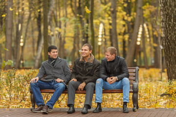 Three young men in black outerwear sitting on park bench and talk