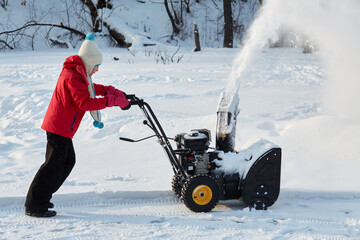 Girl removes snow with gas snow thrower at winter day