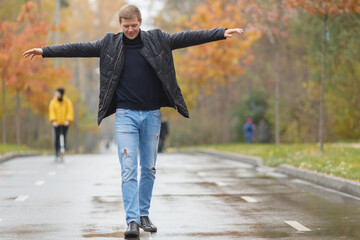 Young man in black jacket is on avenue in park, going straight line, hand in side