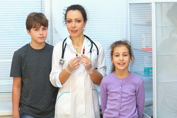 Health worker with syringe and two patients, a boy and a girl, in office of physical therapy, focus on woman © Pavel Losevsky