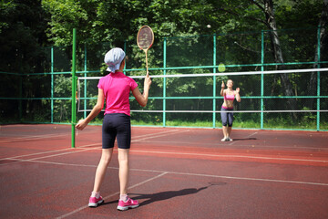 Obraz premium Girl with her mother play tennis on the tennis court, view from the back