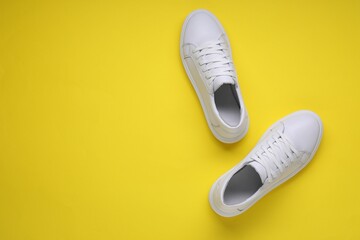 Pair of stylish white sneakers on yellow background, top view. Space for text