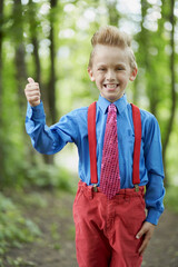 Portrait of grinning boy showing thumb up in summer park