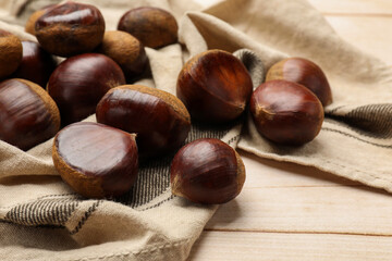 Sweet fresh edible chestnuts on light wooden table, closeup