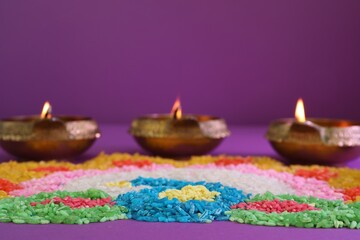 Diwali celebration. Diya lamps and colorful rangoli on purple background, closeup