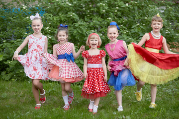 Five smiling little girls dressed in dancing suits pose at grassy lawn