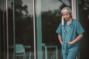 Tired depressed female asian scrub nurse wears face mask blue uniform sits on hospital floor,Young...