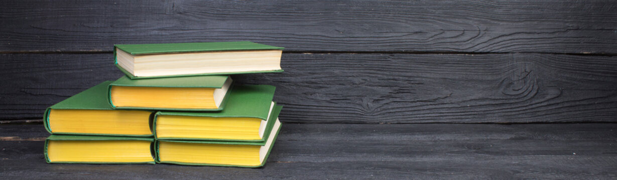 Books on wooden table, black board background. Back to school. Education business concept. panorama, banner.