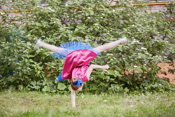 Little girl in dancing suit stands on one arm upside down at grassy lawn
