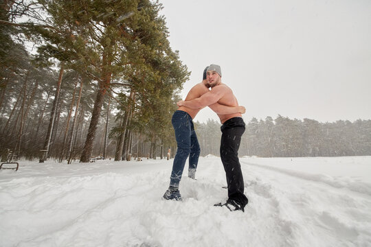 Two bare-chested guys wrestle standing at outdoor sportsground in winter wood