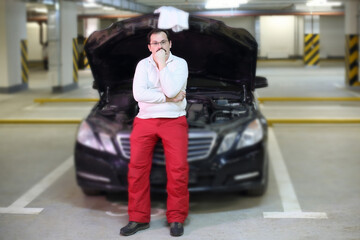 Pensive man with a mustache sitting near the open hood of the car in the underground parking