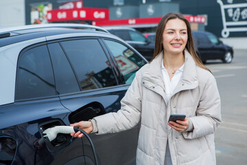 Young woman charging her electric car at a charging station in the city. Eco fuel concept. The concept of environmentally friendly transport. Recharging battery from charging station.