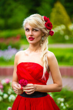 Half length portrait of beautiful woman in red dress with rose in her hands in summer park