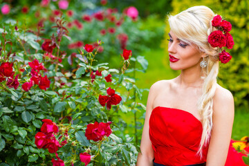 Half length portrait of beautiful woman in red dress in summer park sitting on grass and looking at flowers