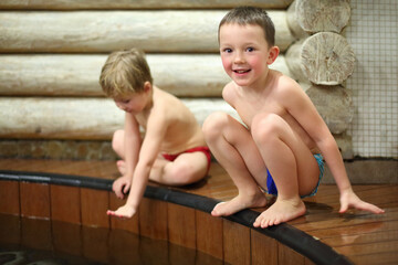 Two happy little boys sitting near the wooden pool in the sauna